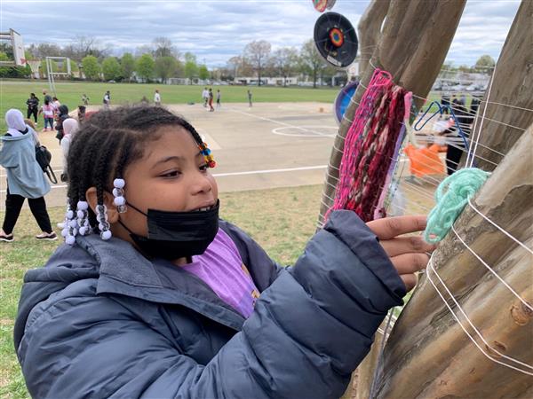 Student engaging in outdoor visual art project with yarn